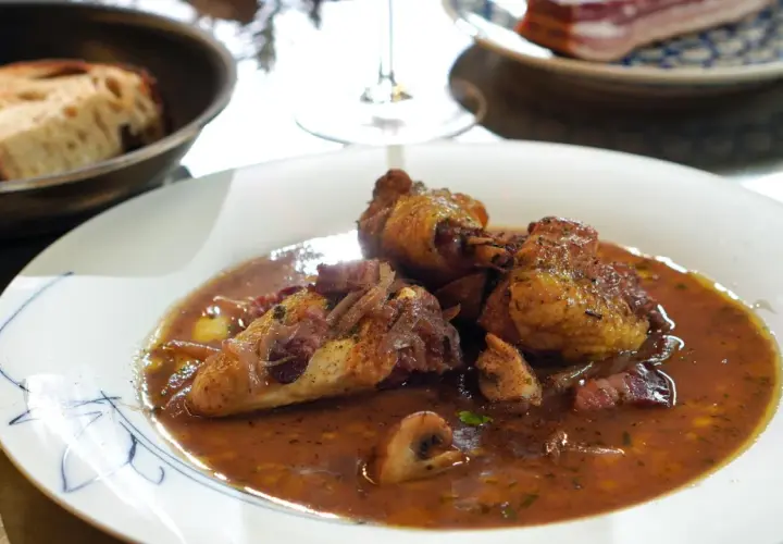 Ein köstliches Coq au Vin Rezept: zartes Hähnchen in Rotwein-Sauce mit Speck und Pilzen, serviert mit Brot.