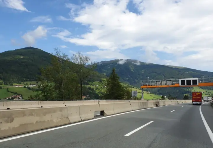 Autostrada w Austrii z widokiem na góry, znaki drogowe i ciężarówka.
