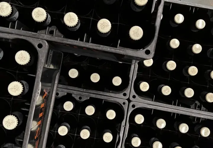 Bouteilles noires empilées dans des casiers, prêtes pour la fermentation haute. Les capsules crème arborent un motif discret.