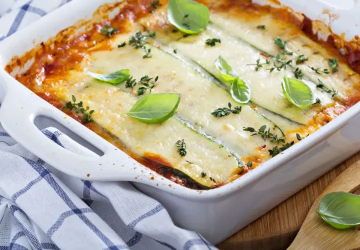 Pyszne lasagne z cukinią, zapieczone pod ciągnącym serem, ozdobione świeżą bazylią i tymiankiem.