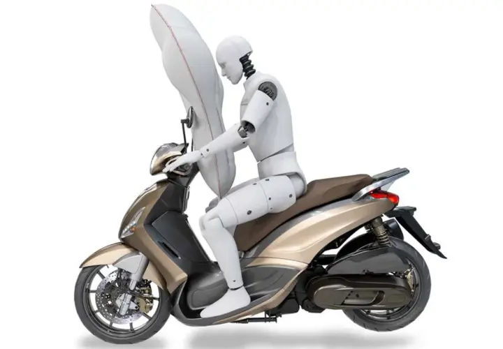 Un maniquí en una moto dorada con un airbag inflado protegiendo su torso. Las motos tienen airbag para mayor seguridad.