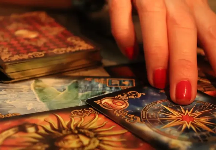 Dłoń z czerwonymi paznokciami nad kartami tarota. Widoczna karta z gwiazdą i znaki zodiaku, sugerująca tarot ryby miesięczny.