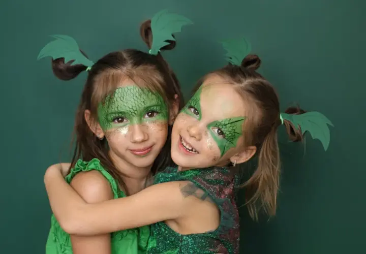 Zwei Mädchen mit Drachenschminke und grünen Flügeln im Haar, ein einfaches Drachen-Kinderschminken-Ergebnis.