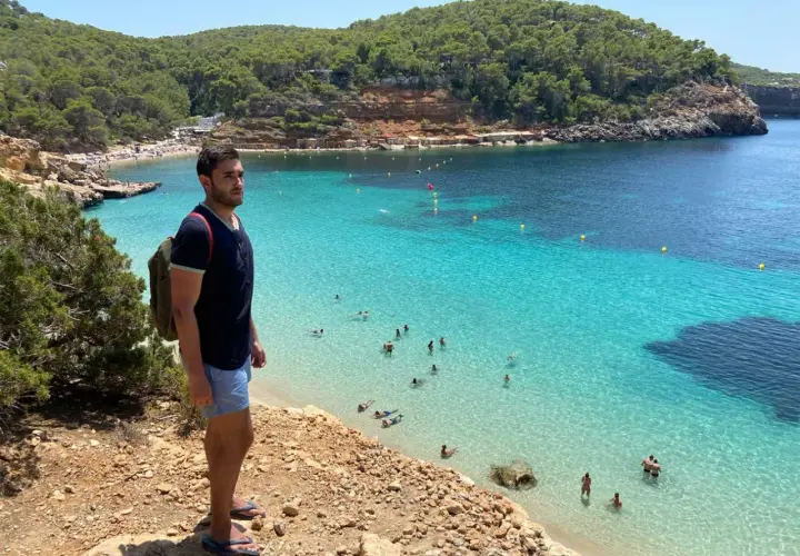Un hombre con mochila admira una cala turquesa en Ibiza. ¡Un plan perfecto que ver en Ibiza en 4 días!