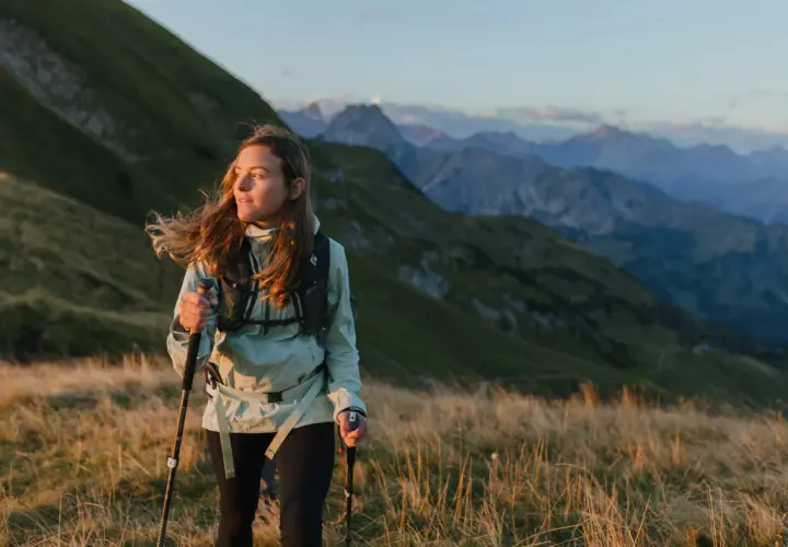 Kobieta z kijkami do speed hiking podziwia górski krajobraz o zachodzie słońca.