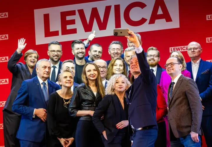 Grupa polityków Lewicy pozuje do selfie na tle czerwonej ściany z logo partii.