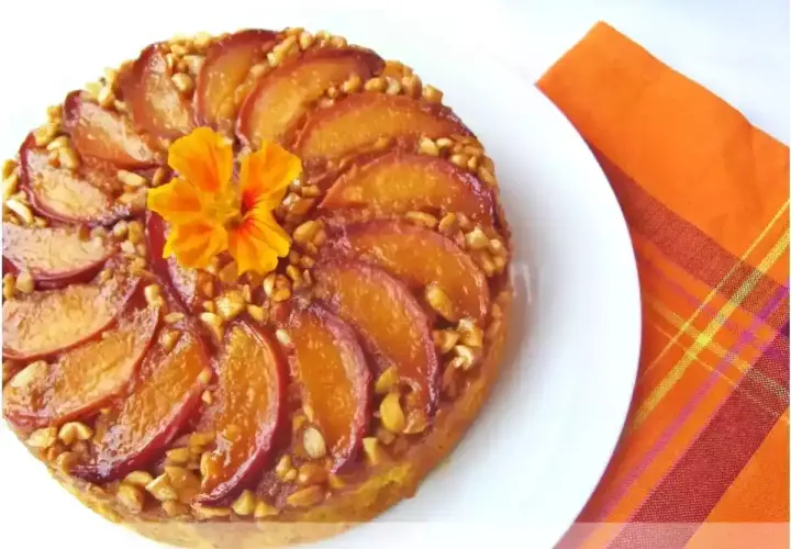 Deliziosa torta di pesche rovesciata, con pesche caramellate, noci croccanti e un fiore arancione al centro.