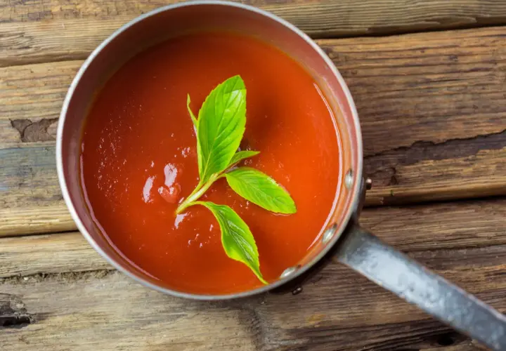 Frische, hausgemachte tomatensauce aus reifen Tomaten, garniert mit Basilikum, in einem Topf auf rustikalem Holz.