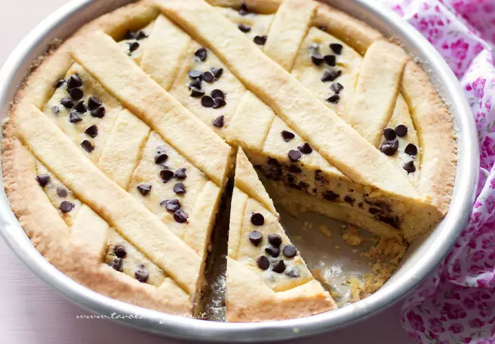 Deliziosa crostata ricotta e gocce di cioccolato, con una fetta tagliata per mostrare il ripieno cremoso e le gocce scure.