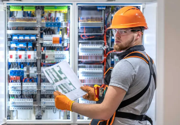 Elektryk z uprawnieniami SEP G1 sprawdza schemat przy rozdzielnicy elektrycznej.