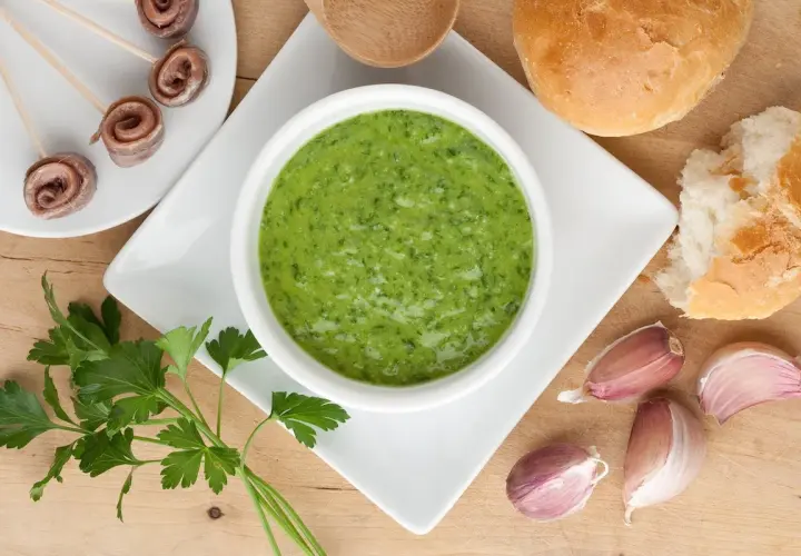 Salsa verde ricetta: prezzemolo fresco, aglio, acciughe arrotolate e pane croccante, ingredienti per un sapore intenso.