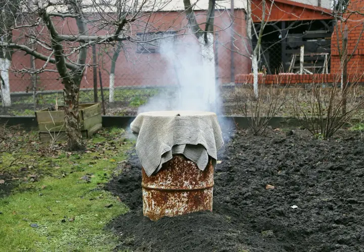 Dym unosi się z rustykalnej wędzarni z beczki, która stoi na ziemi w ogrodzie.