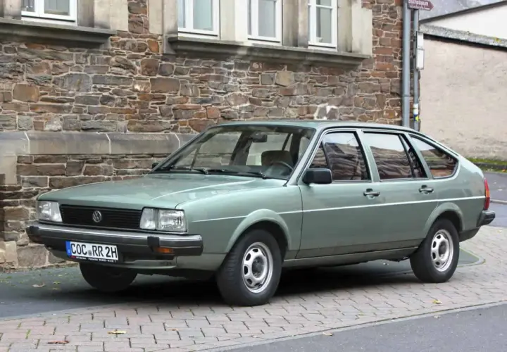 Zielonawy Volkswagen Passat, klasyk z lat 80., parkuje przed kamiennym budynkiem.