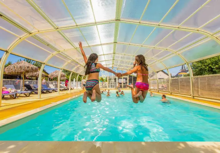 Deux filles sautent main dans la main dans une piscine couverte. Vacances en camping-car à Saint-Malo.