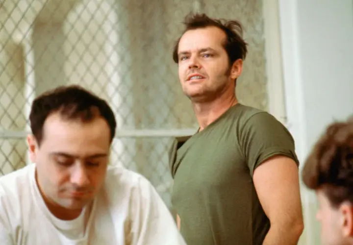 Jack Nicholson, con sguardo intenso, incarna la ribellione nel film "Qualcuno volò sul nido del cuculo", sfidando l'autorità in un contesto di reclusione.