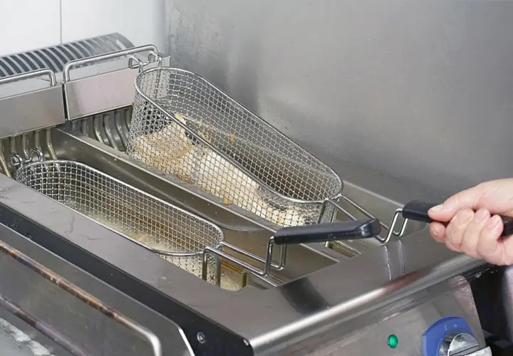 Frytki smażące się w metalowych koszach we frytkownicy.