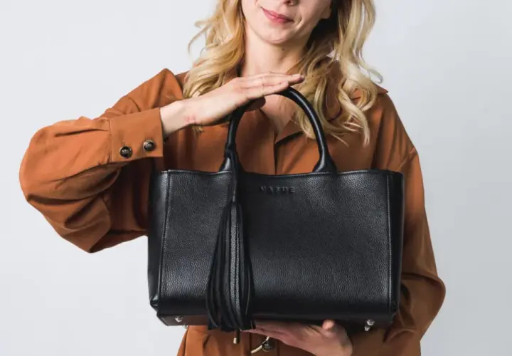 Elegancka, czarna torebka z frędzlem, idealna jako modne torebki na lato. Kobieta w rudym kombinezonie prezentuje stylowy dodatek.