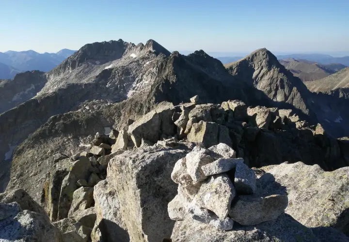 Cumbre rocosa con cairn, vista panorámica de montañas escarpadas bajo cielo azul. Besiberri Nord.