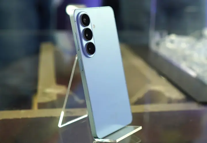 Jasnoniebieski Samsung Galaxy S26 z potrójnym aparatem z tyłu, stojący na przezroczystej podstawce.