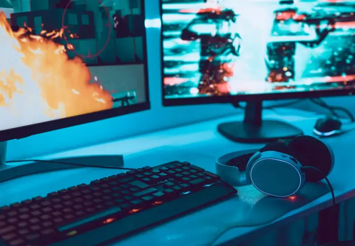 Gaming-Setup mit zwei Monitoren, Tastatur und Kopfhörern. Auf dem linken Bildschirm lodert Feuer, rechts sind Charaktere zu sehen. Perfekt für VA oder IPS.