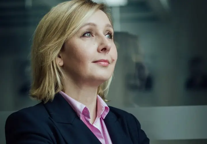 Blond polityk w różowej koszuli i granatowej marynarce patrzy w bok. W tle rozmyte sylwetki innych polityków.