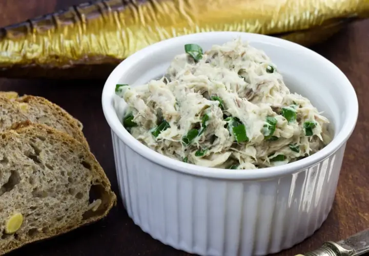 Pyszna pasta z makreli i twarogu, posypana szczypiorkiem, obok kromek chleba i wędzonej makreli.