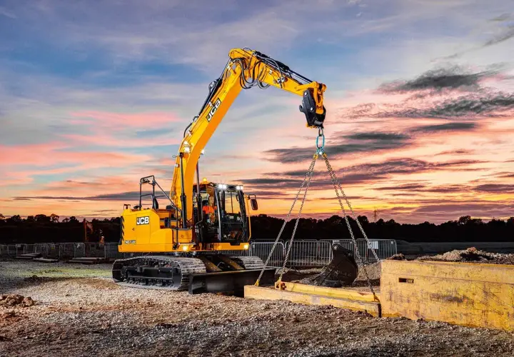 Operator koparki kurs: żółta maszyna JCB podnosi ciężki element na tle zachodzącego słońca.