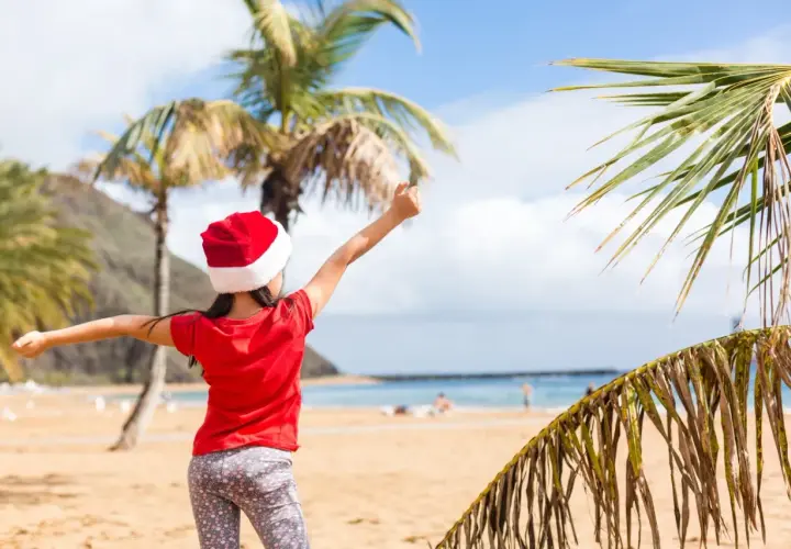 Dziewczynka w czapce Mikołaja cieszy się plażą i palmami. To wyjątkowe boże narodzenie w ciepłych krajach, gdzie śnieg zastępuje piasek.