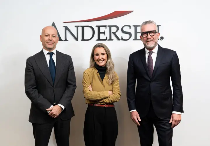 Tres personas posan frente al logo de Andersen. El hombre de la izquierda, calvo, viste traje gris. La mujer del centro, con brazos cruzados, lleva una blusa ocre. El hombre de la derecha, con gafas, viste traje oscuro. Un momento clave, como un ejempl...