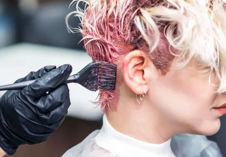 Manos enguantadas aplican tinte rosa al cabello. Si te manchas, aprende como quitar el tinte de la piel.