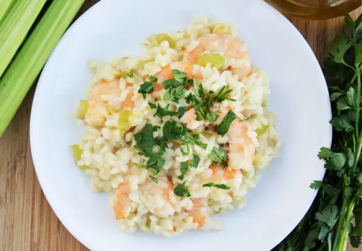 Pyszne risotto z krewetkami, udekorowane natką pietruszki, obok łodygi selera i oliwy.