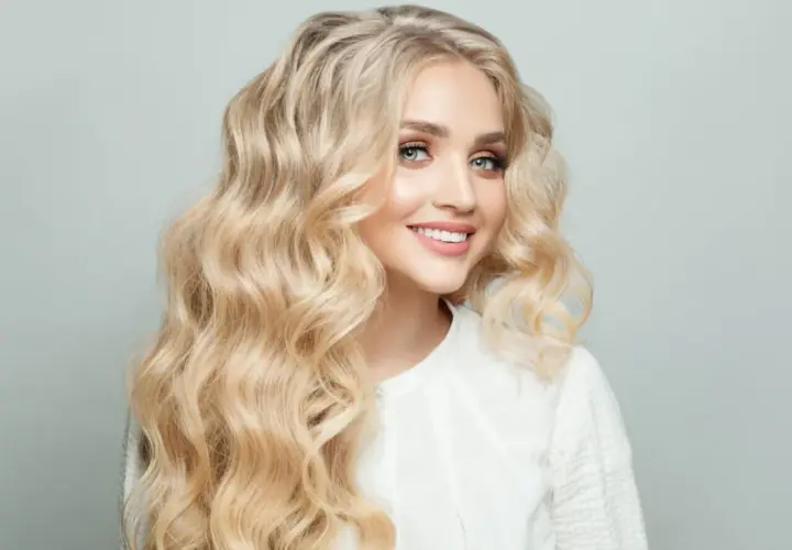 Mujer sonriente con cabello rubio mantequilla ondulado y ojos azules brillantes.