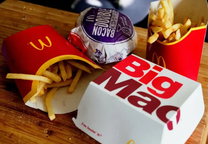 Frytki z McDonald's w czerwonych opakowaniach obok pudełka Big Mac i burgera.