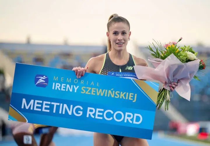 Uśmiechnięta lekkoatletka z bukietem kwiatów trzyma tablicę "MEETING RECORD" z logo memoriału Ireny Szewińskiej.