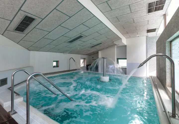 Piscina de hidromasaje con chorros de agua y cascada central en un balneario.