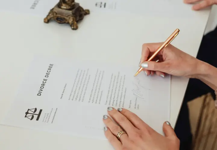 Dłoń podpisuje dokument "DIVORCE DECREE". Dowiedz się, jak napisać pozew o rozwód bez orzekania o winie.
