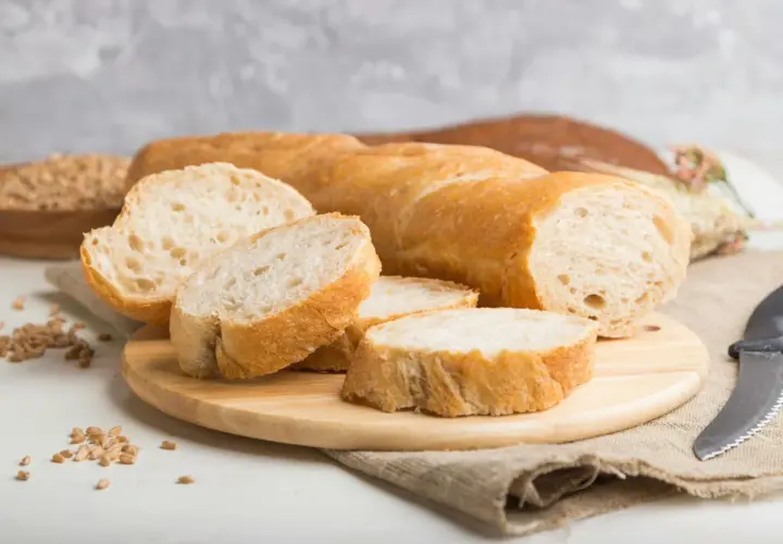 Aufgeschnittenes Baguette auf Holzbrett mit Weizenkörnern und Messer.