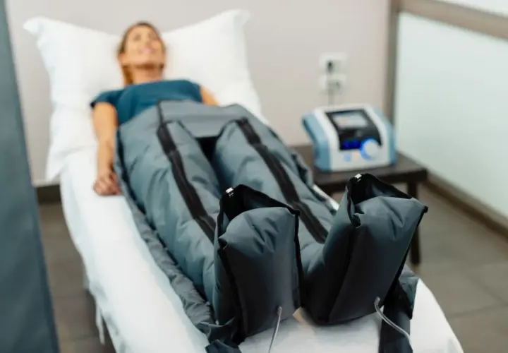 Kobieta leży na łóżku, jej nogi są w specjalnych mankietach. To presoterapia, zabieg poprawiający krążenie.