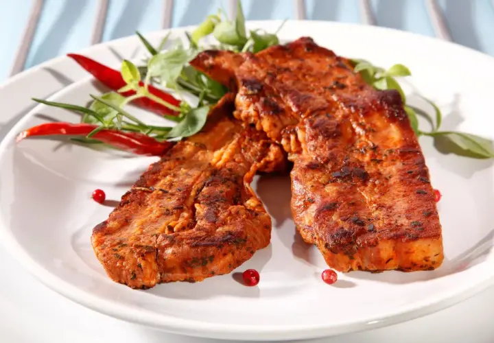 Dwa soczyste plastry boczku na grilla, przyprawione i udekorowane papryczkami chili i zieleniną.