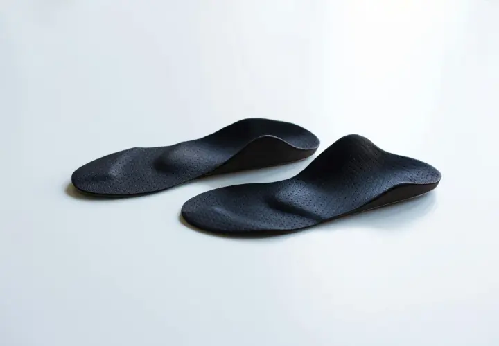 Zwei schwarze, ergonomisch geformte sensomotorische Schuheinlagen liegen auf weißem Untergrund.