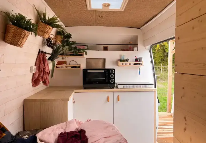 Aménagement intérieur d'un van aménagé : cuisine fonctionnelle avec four, plaque de cuisson, rangements et touches végétales.
