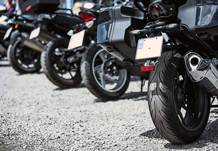 Varias motos aparcadas en fila, una moto sin matrícula visible en primer plano, con su rueda trasera y maleta.