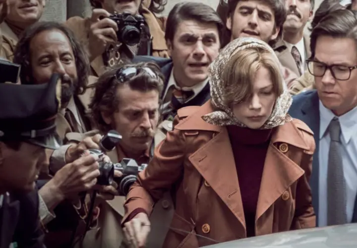 Otoczona przez paparazzi, kobieta w brązowym płaszczu i mężczyzna w okularach wyglądają, jakby chcieli zdobyć wszystkie pieniądze świata, by uciec od tej uwagi.