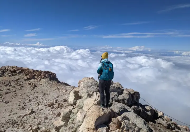 Widok z góry na chmury, osoba z plecakiem i kijkami trekkingowymi na skalistym szczycie. To wspaniałe wejście na Teide!