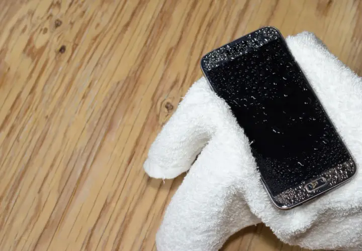 Telefon Samsung z kroplami wody na ekranie, owinięty w biały ręcznik. Jak wyłączyć czujnik wilgoci Samsung, gdy telefon jest mokry?
