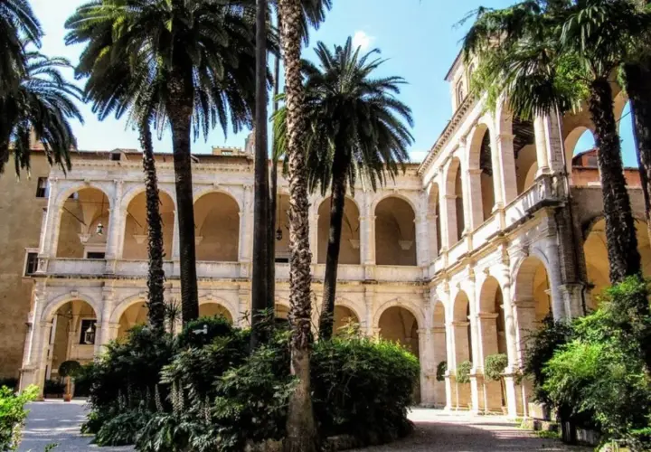 Cour intérieure avec palmiers, arcades et balcons, évoquant le Vittoriano et le Palazzo Venezia.