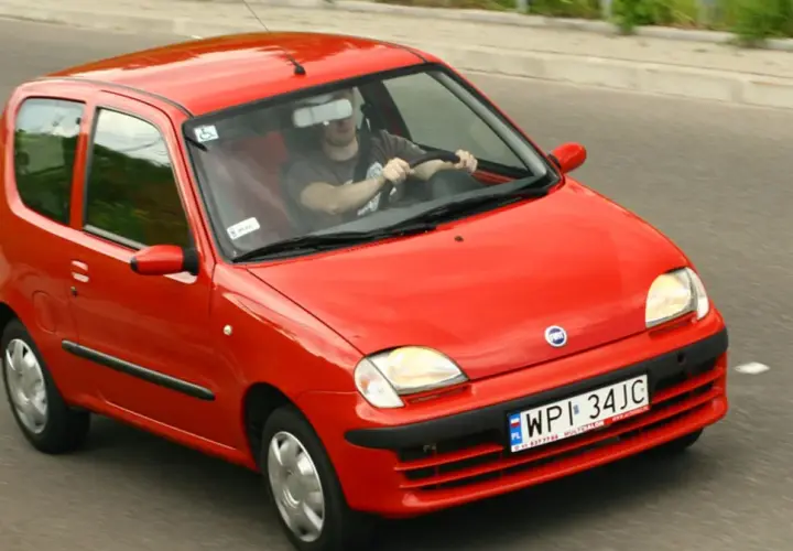 Czerwone Fiat Seicento w ruchu drogowym, widok z przodu i z boku.