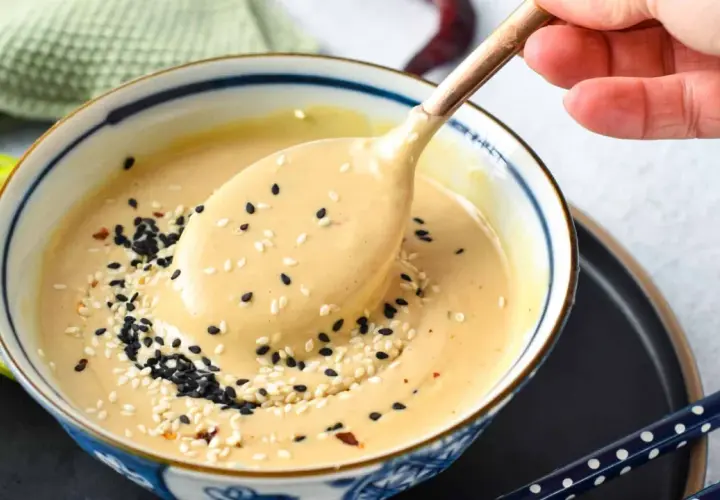 A creamy tahini dressing, sprinkled with black and white sesame seeds, is scooped from a bowl. This tahini sauce is a delicious alternative to miso for many dishes.