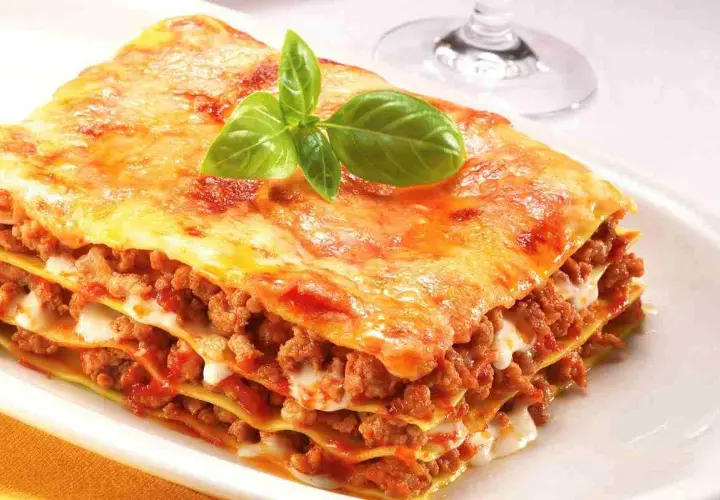 Porzione di lasagne fatte in casa, stratificate con ragù e besciamella, guarnite con basilico fresco.