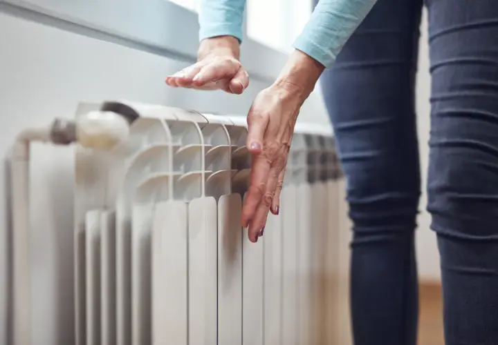 Dłoń sprawdza temperaturę grzejnika, który nie grzeje na dole.